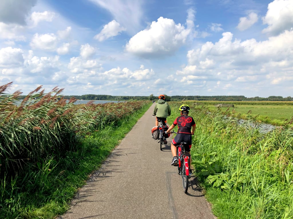 Cicloturisti su pista ciclabile tra canali e campi verdi nella campagna dei Paesi Bassi